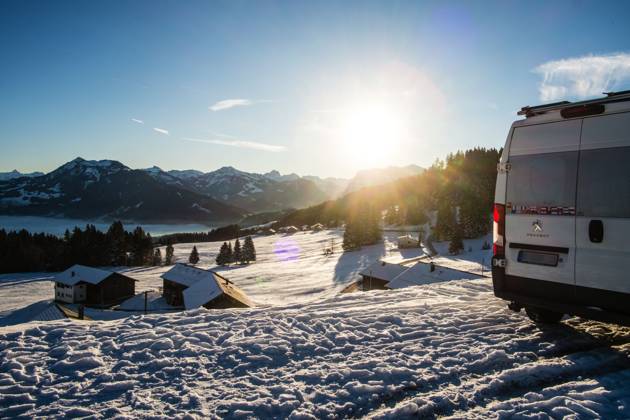 Ein Camper steht im Winter auf einem Parkplatz in den Alpen bei Sonnenaufgang im Schnee. Bödele, Vorarlberg, Österreich Winter in den österreichischen Alpen