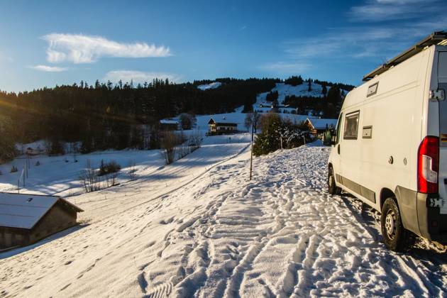 Ein Camper steht im Winter auf einem Parkplatz in den Alpen bei Sonnenaufgang im Schnee. Bödele, Vorarlberg, Österreich Winter in den österreichischen Alpen
