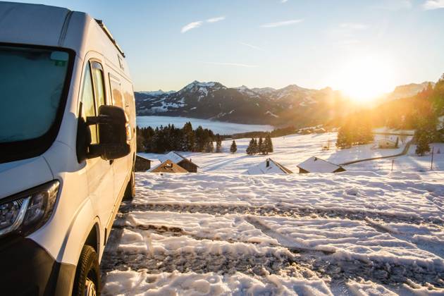 Ein Camper steht im Winter auf einem Parkplatz in den Alpen bei Sonnenaufgang im Schnee. Bödele, Vorarlberg, Österreich Winter in den österreichischen Alpen