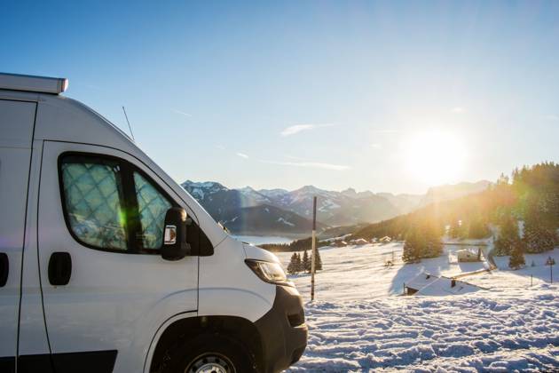 Ein Camper steht im Winter auf einem Parkplatz in den Alpen bei Sonnenaufgang im Schnee. Bödele, Vorarlberg, Österreich Winter in den österreichischen Alpen