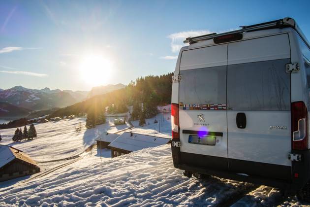 Ein Camper steht im Winter auf einem Parkplatz in den Alpen bei Sonnenaufgang im Schnee. Bödele, Vorarlberg, Österreich Winter in den österreichischen Alpen