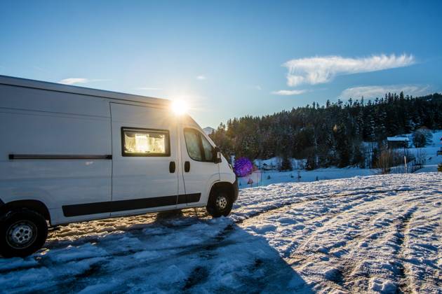 Ein Camper steht im Winter auf einem Parkplatz in den Alpen bei Sonnenaufgang im Schnee. Bödele, Vorarlberg, Österreich Winter in den österreichischen Alpen