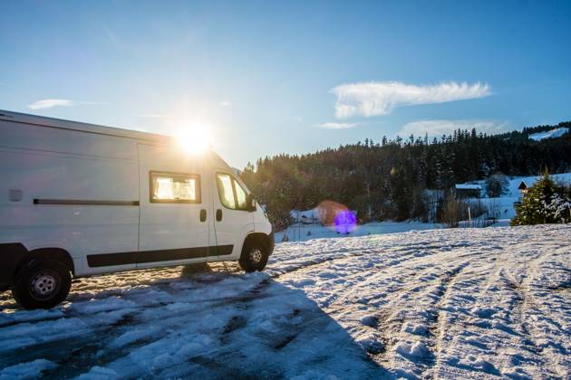 Ein Camper steht im Winter auf einem Parkplatz in den Alpen bei Sonnenaufgang im Schnee. Bödele, Vorarlberg, Österreich Winter in den österreichischen Alpen