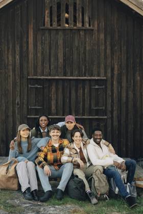 Portrait of happy multiracial male and female friends sitting with arm around each other in front of log cabin Sweden, Gothenburg, model released, property released Copyright: xMaskotx , MA114972 MA114972
