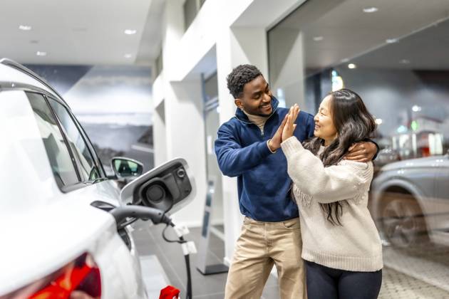 Ein glückliches multiethnisches Paar feiert den Kauf seines neuen Elektroautos mit einem High Five im Autohaus und strahlt vor Freude und Begeisterung Happy multiethnic couple celebrating their new electric car purchase with a high five at the dealership, radiating joy and excitement Copyright: imageBROKER UnaixHuizi ibxuhu12460363.jpg ,model released, Symbolfoto ,property released