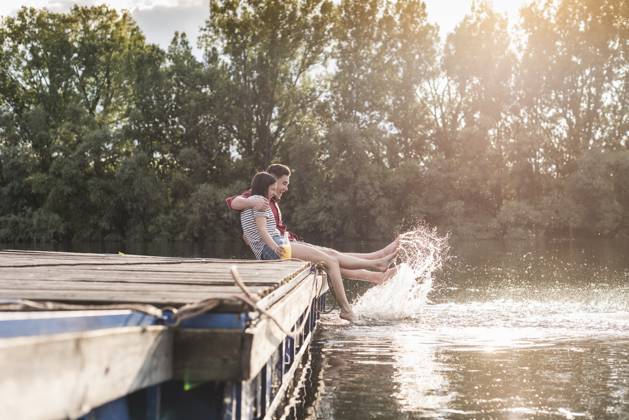Happy young couple having a drink and splashing with water on jetty at a remote lake model released, Symbolfoto, UUF17938