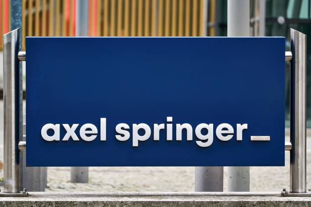 Blaues Schild mit weißem axel springer Schriftzug vor dem Axel-Springer-Hochhaus in Berlin