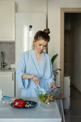 MR_ID27929_20617_TatyanaRangulova.jpg, PR_ID27929_10891_Cat.jpg, PR_ID27929_10892_Room.jpg A woman in a light blue robe mixes a fresh salad in a modern kitchen. Surrounded by vibrant vegetables, she embodies a calm and healthy home lifestyle., Property released Model Released LiliyaSolopova_ID27929_802064_008 Copyright: xLiliyaxSolopovax