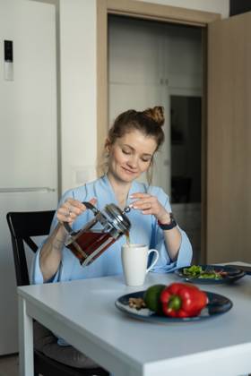 MR_ID27929_20617_TatyanaRangulova.jpg, PR_ID27929_10891_Cat.jpg, PR_ID27929_10892_Room.jpg A woman in a casual setting pours tea into a mug at her kitchen table, creating a warm and cozy atmosphere. Fresh vegetables are seen on the table, enhancing the homely vibe., Property released Model Released LiliyaSolopova_ID27929_802066_010 Copyright: xLiliyaxSolopovax