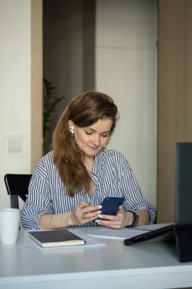 MR_ID27929_20617_TatyanaRangulova.jpg, PR_ID27929_10891_Cat.jpg, PR_ID27929_10892_Room.jpg Young woman in casual attire, engaged in work or study from home, using a smartphone and laptop at a table. AirPods and a notebook suggest productivity and focus., Property released Model Released LiliyaSolopova_ID27929_802070_013 Copyright: xLiliyaxSolopovax
