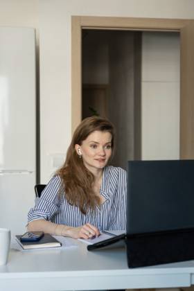 MR_ID27929_20617_TatyanaRangulova.jpg, PR_ID27929_10891_Cat.jpg, PR_ID27929_10892_Room.jpg A woman in a striped shirt works on a laptop at home, engaging in a virtual meeting. She appears focused and attentive, using earbuds and taking notes with a notebook nearby., Property released Model Released LiliyaSolopova_ID27929_802078_018 Copyright: xLiliyaxSolopovax