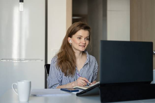 MR_ID27929_20617_TatyanaRangulova.jpg, PR_ID27929_10891_Cat.jpg, PR_ID27929_10892_Room.jpg A woman sits at a table working remotely from home. She writes in a notebook while focusing on her laptop screen, with a mug and phone nearby., Property released Model Released LiliyaSolopova_ID27929_802080_019 Copyright: xLiliyaxSolopovax