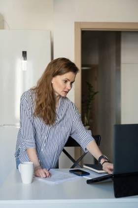 MR_ID27929_20617_TatyanaRangulova.jpg, PR_ID27929_10891_Cat.jpg, PR_ID27929_10892_Room.jpg A woman dressed casually in stripes works from home, standing at a table with a laptop, papers, and a phone, illustrating modern remote work and concentration., Property released Model Released LiliyaSolopova_ID27929_802082_021 Copyright: xLiliyaxSolopovax