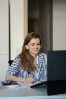 MR_ID27929_20617_TatyanaRangulova.jpg, PR_ID27929_10891_Cat.jpg, PR_ID27929_10892_Room.jpg A woman sitting at her desk at home, smiling as she looks at her laptop screen. She is wearing earbuds, suggesting remote communication or entertainment., Property released Model Released LiliyaSolopova_ID27929_802083_022 Copyright: xLiliyaxSolopovax