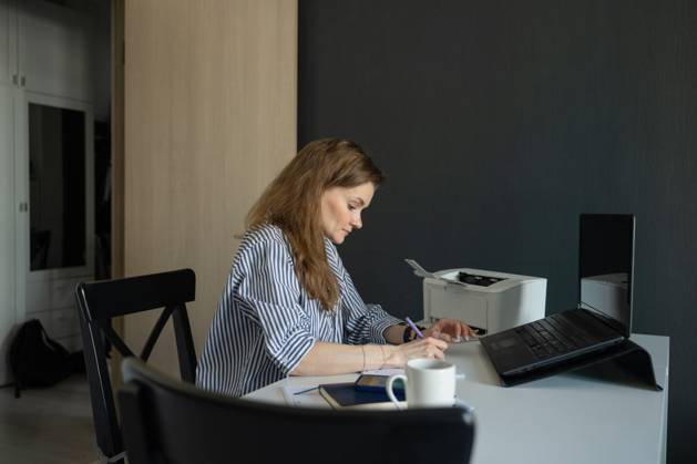 MR_ID27929_20617_TatyanaRangulova.jpg, PR_ID27929_10891_Cat.jpg, PR_ID27929_10892_Room.jpg A woman in a striped shirt works at home, focusing on writing in a notebook beside a laptop. A cup of coffee and a printer are visible on the desk. The atmosphere is calm and productive., Property released Model Released LiliyaSolopova_ID27929_802085_023 Copyright: xLiliyaxSolopovax