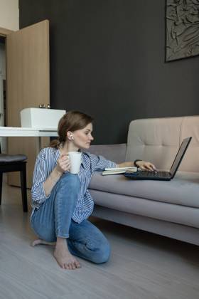 MR_ID27929_20617_TatyanaRangulova.jpg, PR_ID27929_10891_Cat.jpg, PR_ID27929_10892_Room.jpg A woman sitting on the floor by a sofa, working on a laptop. She holds a coffee mug and listens with earbuds. The atmosphere is cozy and relaxed at home., Property released Model Released LiliyaSolopova_ID27929_802099_032 Copyright: xLiliyaxSolopovax