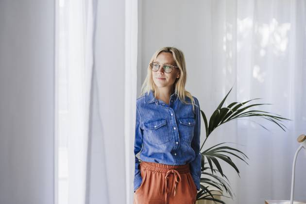 Young woman with hands in pockets standing by window at home model released, Symbolfoto property released, EBBF05770