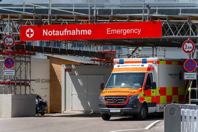 Ein Rettungswagen steht vor dem Eingang einer Notaufnahme mit deutlich sichtbarer Beschilderung auf Deutsch und Englisch, vor einem modernen Krankenhaus