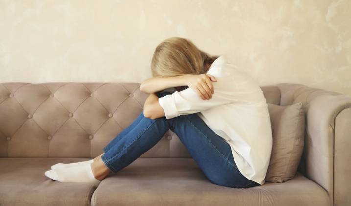 Aufgewühlte, traurige, weinende Frau, die ihre Augen und ihr Gesicht mit den Händen bedeckt, während sie seelisches oder körperliches Leid erfährt, Müdigkeit, die auf der Couch in einem Zimmer zu Hause sitzt Upset sad crying woman covering her eyes and face with her hands while experiencing mental or physical suffering, fatigue sitting on the couch in room at home Copyright: imageBROKER VeronikaxKorneva ibxiqx14269930.jpg ,model released, Symbolfoto ,property released