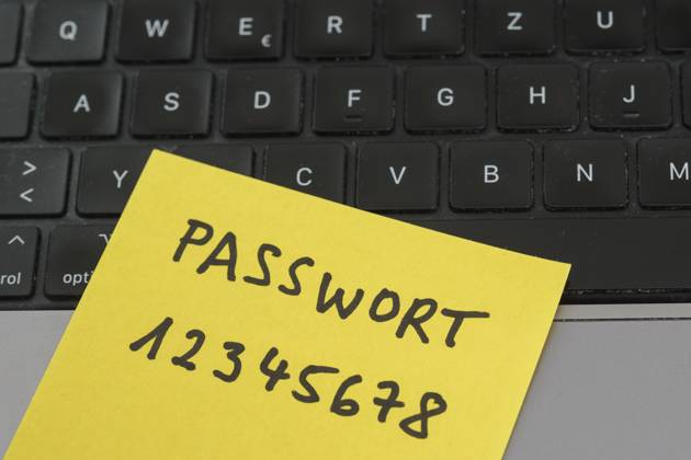 Sicherheitsrisiko auf dem Schreibtisch: Ein Zettel mit dem unsicheren Passwort 12345678 liegt offen auf einem Laptop, ein klassisches Beispiel für fahrlässigen Umgang mit sensiblen Zugangsdaten.