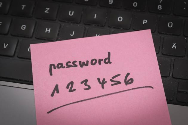 Sicherheitsrisiko auf dem Schreibtisch: Ein Zettel mit dem unsicheren Passwort 123456 liegt offen auf einem Laptop, ein klassisches Beispiel für fahrlässigen Umgang mit sensiblen Zugangsdaten.
