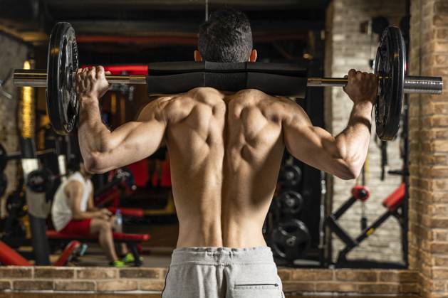 Rückenansicht eines jungen Bodybuilders, der seine Muskeln mit einer Langhantel vor einem Spiegel im Fitnessstudio anspannt Back view of young bodybuilder flexing muscles with barbell in front of mirror at gym Copyright: imageBROKER Dr.xMartinxBaumgärtn ibxiqx14302823.jpg ,model released, Symbolfoto ,property released