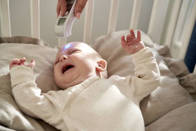 Mother checking temperature of crying baby lying in crib at home model released, Symbolfoto, ABIF01984