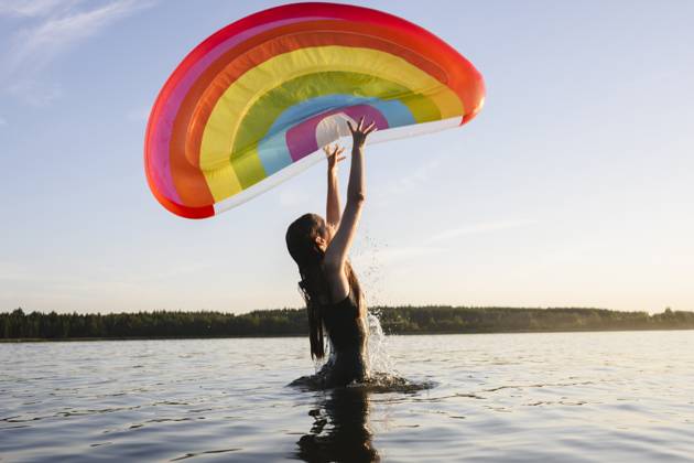 Person in swim suit playing with rainbow float in lake during summer model released, Symbolfoto, EYAF03494