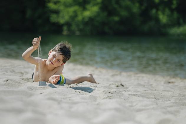 Child lying on sandy beach playing with sand on a summer day model released, Symbolfoto, ANAF04951
