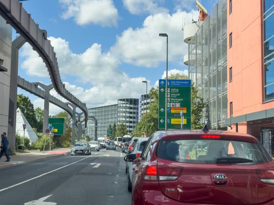 Düsseldorf, Nordrhein-Westfalen, Deutschland, Europa: Verkehrsszene am Flughafen Düsseldorf, Zufahrt zu Terminal und Parkhäusern, Wegweiser für Abflug, Ankunft, Mietwagen, Stau und Reiseverkehr, Flughafeninfrastruktur, SkyTrain-Trasse, moderne Architektur, Mobilität, Luftfahrt, Pendelverkehr, Infrastruktur Deutschland, Urlaubsreisen. Copyright: xJOERANxSTEINSIEKx