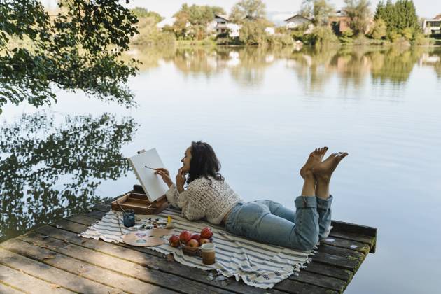 Person painting and relaxing on dock by scenic lake outdoors model released, Symbolfoto, NDEF02897