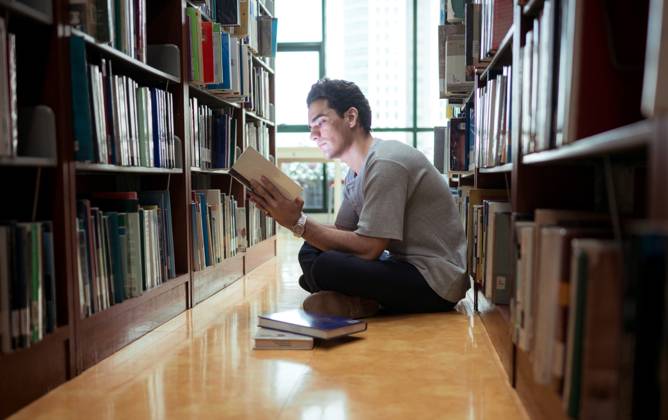 Ein junger Mann sitzt in der Bibliothek und liest konzentriert ein Buch A young man sitting on the library floor reading a book with concentration (License=RF) ,model released, Symbolfoto Copyright: xZoonar.com WosunanxPhotostoryx 24197871 ,model released, Symbolfoto ,property released