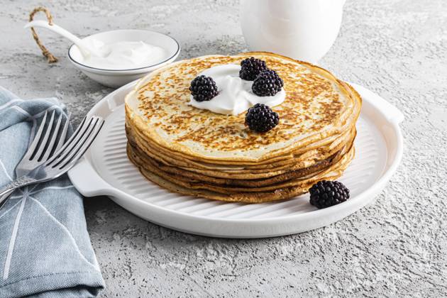 Ein großer Stapel köstlicher heißer Pfannkuchen mit saurer Sahne und Brombeeren auf einem schönen weißen Serviertablett mit Besteck und einem Grundstück. View from front A large stack of delicious hot pancakes with sour cream and blackberries on a beautiful white serving tray with cutlery and a plot. Front view Copyright: imageBROKER MarinaxMoskalyuk ibxiqx14292238.jpg