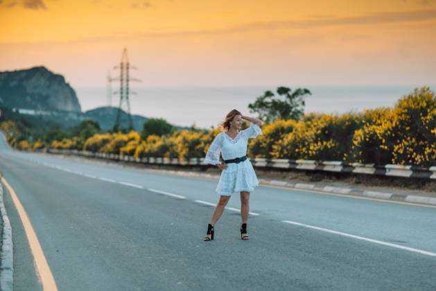 A woman in a white dress is standing on a road, looking at the camera A woman in a white dress is standing on a road, looking at the camera. The scene is set against a backdrop of a beautiful sunset, with the sky turning orange and pink. The woman is enjoying the moment, model released, , 62026546.jpg RECORD DATE NOT STATED