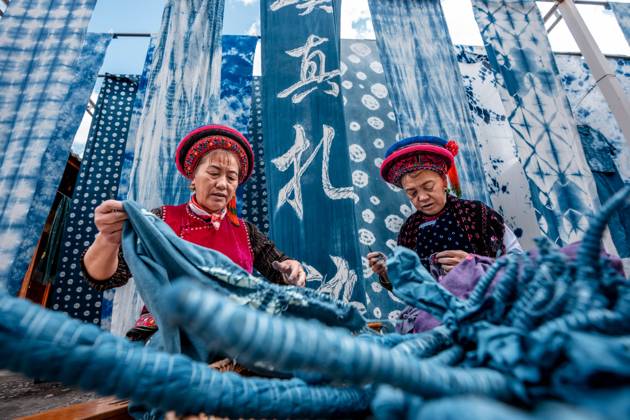 (251122) -- DALI, Nov. 22, 2025 -- Duan Yinmei (L), an inheritor of the tie-dye technique of Bai ethnic group, and handicraftsman Duan Lilan untie knots on fabrics in a dyehouse in Zhoucheng Village of Dali Bai Autonomous Prefecture, southwest China s Yunnan Province, Nov. 21, 2025. Known as the hometown of the tie-dye technique of Bai ethnic group, Zhoucheng Village hosts over 200 households engaging in tie-dye businesses, with the number of employees exceeding 4,000. As a traditional folk technique of the Bai ethnic group, tie-dye boasts a history spanning over a thousand years and was included in the first batch of China s national intangible cultural heritage list in 2006. Tying and dyeing are the core steps in the process of making