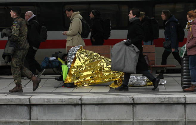 Ein Obdachloser liegt auf einer Sitzbank auf dem Bahnsteig im Hauptbahnhof Hamburg. Reisende gehen an ihm vorbei. St. Georg Hamburg