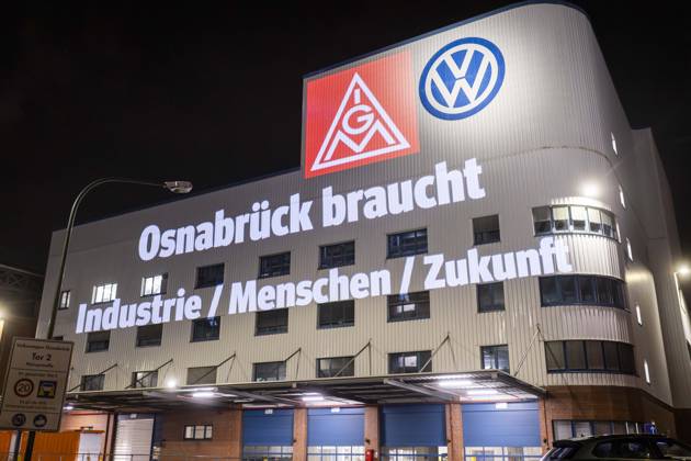 Projektion IG Metall Logo und Schriftzug Osnabrück braucht Industrie Menschen Zukunft neben dem VW Logo an der Fassader des Osnabrücker VW-Werks. Friedliche Protestkundgebung der IG Metall in Osnabück mit zur Situation Automobilbranche VW-Werk Osnabrück. 08.12.2025 IG Metall Kundgebung vor dem VW-Werk Osnabrück