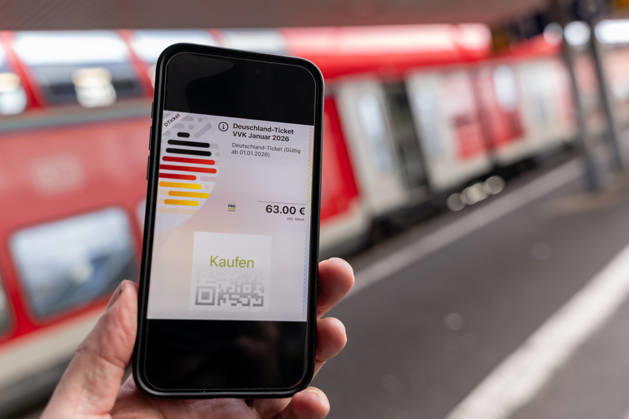 Deutschlandticket mit neuem Preis am Bahnhof 17.12.25, Limburg: Symbolfoto, Illustrationsbild, Symbolbild, Illustrationsfoto, Alltagsszene Ein Smartphone zeigt das digitale Deutschlandticket mit einem Preis von 63 Euro. Das Mobiltelefon wird auf einem Bahnsteig gehalten, im Hintergrund ist ein roter Zug unscharf zu sehen. Das Bild steht im Zusammenhang mit der geplanten Preiserhöhung des Deutschlandtickets zum 1. Januar 2026 sowie mit dem öffentlichen Nahverkehr und dem Bahnverkehr in Deutschland. Limburg Hessen Copyright: xThorstenxWagnerx