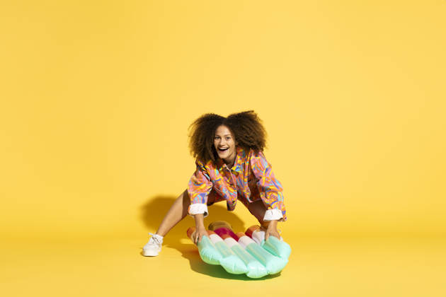 Woman with curly hair holding ice cream shaped pool raft against yellow background model released, Symbolfoto, MIKF00572
