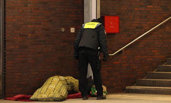 Ein Polizist spricht einen Obdachlosen an, der im Schlafsack im Bahnhof Barmbek liegt. Barmbek Hamburg