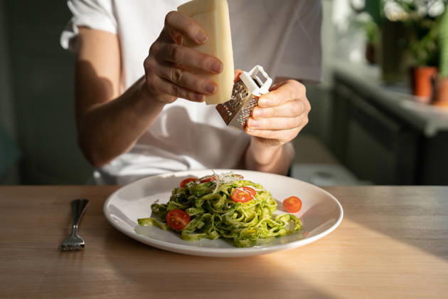 Nahaufnahme von Frauenhänden, die Parmesankäse über Pasta mit Pesto-Sauce und frischen Kirschtomaten reiben. Close up of woman hands grating Parmesan cheese in pasta with sauce pesto, fresh cherry tomatoes, living room on background. Homemade Italian cuisine. (License=RF) ,model released, Symbolfoto Copyright: xZoonar.com DmitriixMarchenkox xEnvatox 24654414 ,model released, Symbolfoto ,property released