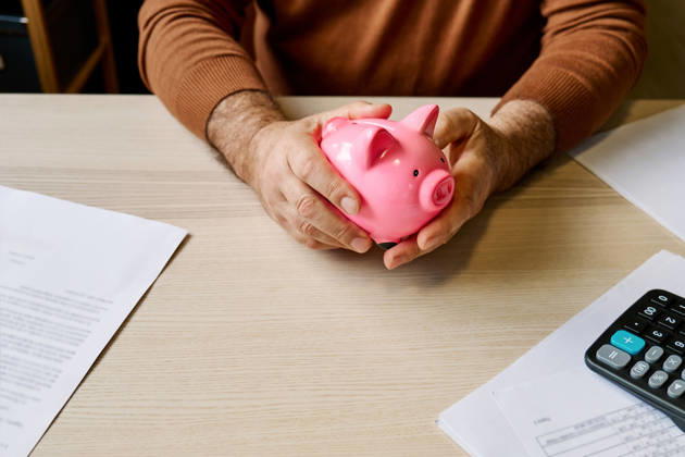 Man holding piggy bank at table with bills and calculator at home model released, Symbolfoto property released, CATF00870