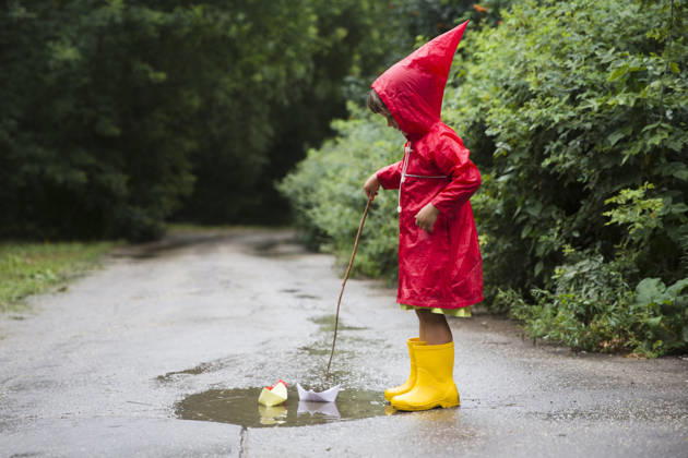 Ein Kind in einem roten Regenmantel und gelben Gummistiefeln spielt nach einem Sommerregen mit Papierbooten in einer Pfütze. a child in red raincoat and yellow rubber boots playing with paper boats in a puddle after rain in the summer (License=RF) ,model released, Symbolfoto Copyright: xZoonar.com UliaxZotaninax 24710694 ,model released, Symbolfoto ,property released
