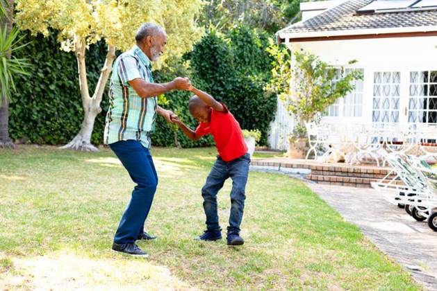 Senior African American man and his grandson spending time together in their garden on a sunny day Senior African American man spending time with his grandson in their garden on a sunny day, teaching him dancing on the lawn., model released, , property released, Cape Town, South Africa, 24.01.2020, 1352260.jpg, people,real people,home,domestic life,lifestyle,free time,leisure,relaxing,happy,enjoying,smiling,summer,garden,backyard,sunny,hobby,heathy,nature,heathy lifestyle,active seniors,retirement,interacting,togetherness,closeness,grandfather,grandson,teaching,learning,dancing,playing,fun Child,Boy,Male,Black,Senior,Elderly,Man,Mixed-Race Outdoors,Side view,Focus on Foreground,Looking Away,Two objects,Day,Full length