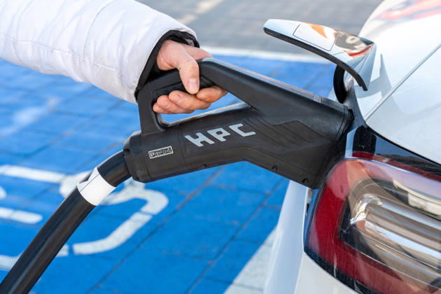 Eine Hand verbindet ein Elektroauto mit einem Schnellladestecker. Die Aufnahme zeigt die einfache Handhabung moderner Ladetechnik im Alltag für eine klimafreundliche Mobilität.