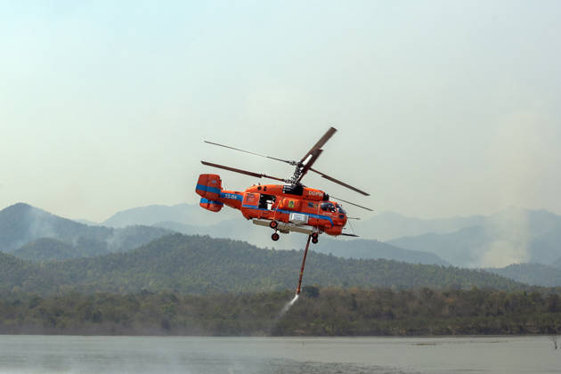 March 27, 2026, Chiang Mai, Thailand: A helicopter performs water pickup operations over a reservoir in Chiang Mai, northern Thailand, as part of aerial firefighting efforts against ongoing wildfires. A KA-32 helicopter from the Department of Disaster Prevention and Mitigation skims the water surface to collect water before heading to fire-affected forest areas amid hazy conditions caused by smoke and rising PM2.5 pollution. Chiang Mai Thailand - ZUMAs197 20260327_aaa_s197_308 Copyright: xPongmanatxTasirix
