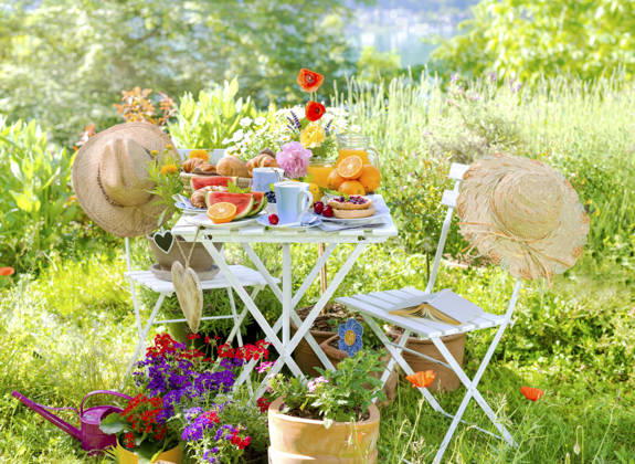 Fruehstueck fuer zwei, angerichtet auf einem Tisch im bunt bluehenden Garten am See mit Sonnenhueten und Herzen, Composing Breakfast for two, served on a table in a colorful garden blooming with coneflowers and hearts, Composing BLWS745584