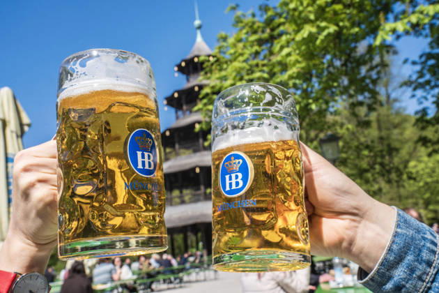 Biergarten am Chinesischen Turm, Frühlingstag im Englischen Garten, zwei Gäste stoßen mit ihrer Mass Bier an, München, April 2026 Deutschland, München, 22. April 2026, Biergarten am Chinesischen Turm, Frühling im Englischen Garten, Temperaturen bis 16 Grad, viele genießen die Sonne bei Bier und einer Brotzeit, zwei Gäste staßen mit ihren Masskrügen an, alles ist grün, Mittwochmittag, Bayern