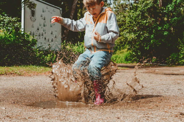 Ein fröhliches Kind springt in wasserdichten Stiefeln durch eine Pfütze. Ein Junge, der voller Spritzwasser ist, spielt in einem herbstlichen Park. A happy child jumps in a puddle in waterproof boots. A boy with splashes is playing in an autumn park. Outdoor activities in rainy weather (License=RF) ,model released, Symbolfoto Copyright: xZoonar.com ElenaxEsichx 24940207 ,model released, Symbolfoto ,property released