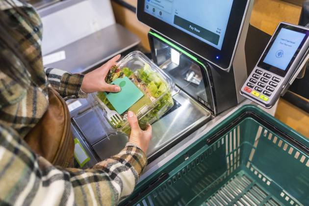 Frau, die einen Selbstbedienungsautomaten benutzt und in einem Lebensmittelgeschäft einen frischen Salat in einem Plastikbehälter scannt, steht für moderne Einzelhandelstechnologie und Einkaufskomfort Woman using a self checkout machine, scanning a fresh salad in a plastic container at a grocery store, representing modern retail technology and shopping convenience Copyright: imageBROKER UnaixHuizi ibxuhu17420427.jpg ,model released, Symbolfoto ,property released